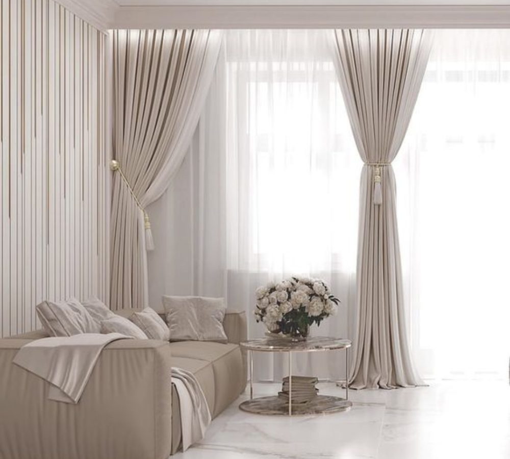 Soggiorno beige con divano vicino alla finestra e tende lunghe